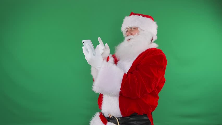 Santa types messages on his phone against a green screen for holiday campaigns.