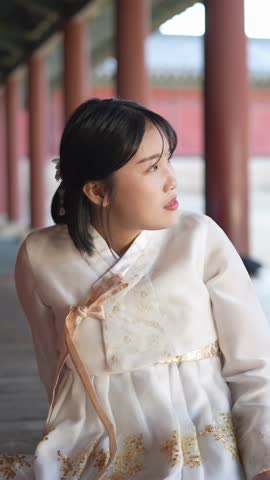A Korean woman in her 20s wearing a Hanbok sits in a historical building in Seoul, South Korea. Vertical video.