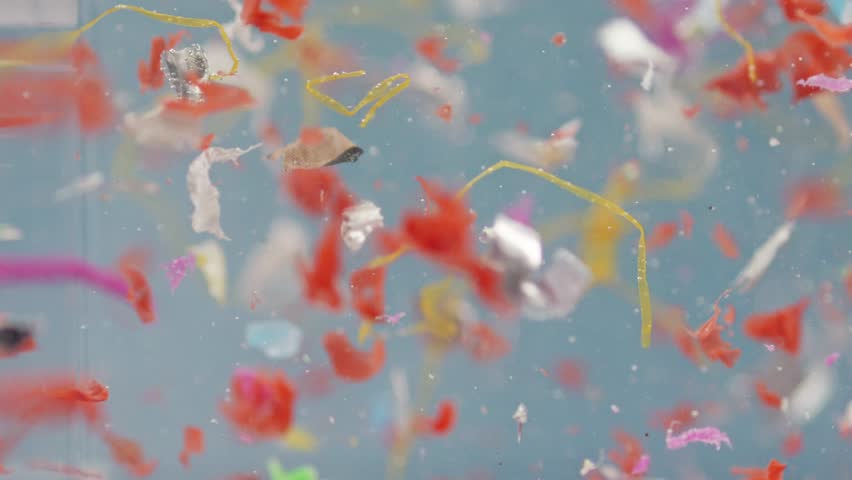 Small microplastic bits float in water in slow motion, showing environmental impact and lab testing on waste pollution.