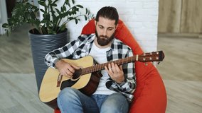Talented musician playing acoustic guitar at home. Professional freelancer enjoys music in cozy apartment. Young man making melody indoors. - Powered by Shutterstock - Get 15% off with code: PIKWIZARD15