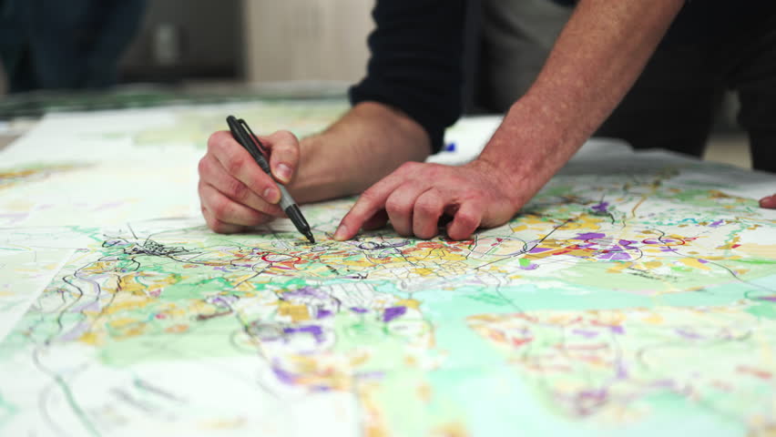 Man surrounded by team uses marker to jot down notes on map. Employees of institute define section of land for future urbanization