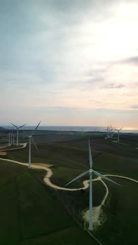 vertical drone captures an aerial view of a wind mill turbine farm with the vast ocean stretching out in the background, emphasizing the fusion of renewable energy and nature