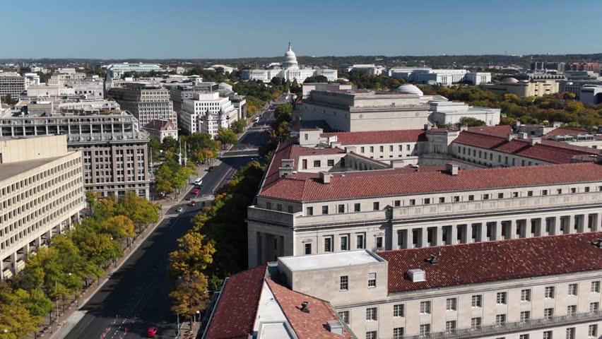 Aerial view of Washington DC featuring a cityscape with various buildings, including the iconic Capitol Building, a street lined with trees, and a large government building with a tiled roof.