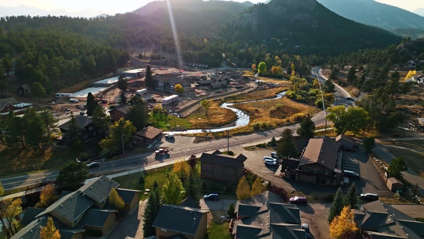 Aerial drone establishing pan over Estes Park, Colorado, scenic autumn foliage with sunflare over mountain valley and meandering river