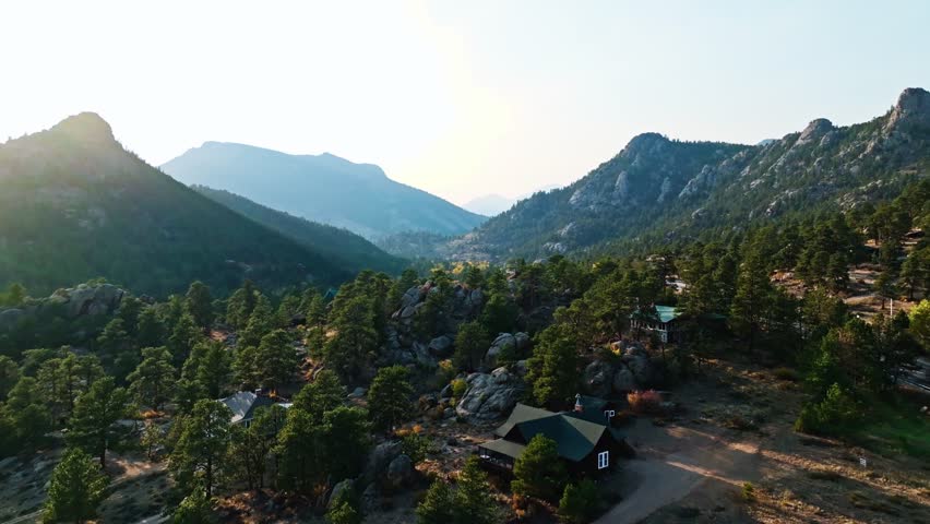 Aerial ascend over mountains and rocky boulders of Estes Park, Colorado, with vibrant autumn colors and sunflare over valley roads and mountain ridges