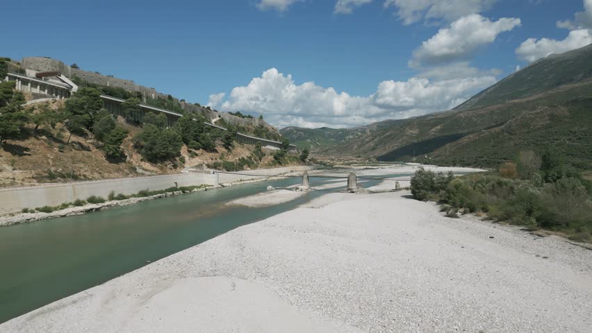 Ali Pasha Bridge in Tepelena, Albania spans turquoise river surrounded by mountains and rocky shore