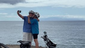 Happy senior couple of cyclists wearing helmets take a selfie with phone enjoying riding seaside with electric bicycles in a sunny day. Healthy lifestyle in retirement. Horizon over the sea - Powered by Shutterstock - Get 15% off with code: PIKWIZARD15
