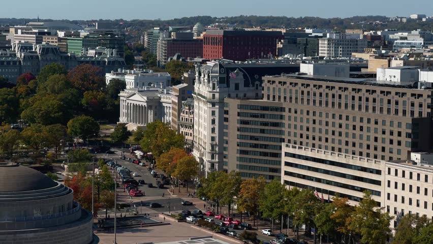 A aerial view of Washington DC cityscape with White House, US Treasury, government buildings, trees, and cars. The view includes a street, and multiple trees with fall foliage.