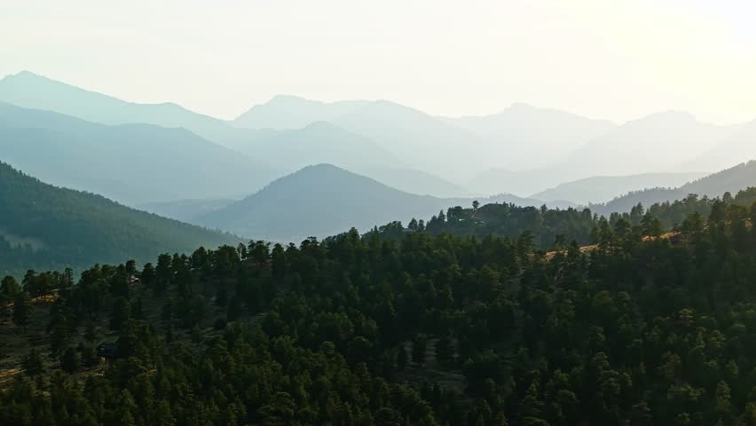 Scenic aerial trucking pan over Estes Park, Colorado, autumn colors and sunlight casting across mountains, stunning layers of ridges off into distance, telephoto compression