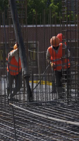 Vertical video. Team of construction workers pouring and leveling concrete on a reinforced foundation, wearing safety gear, emphasizing teamwork and precision.