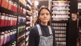 Confident young woman smiling in an art supply store while standing near colorful paint tubes. She can be portrayed as an artist, customer, or employee browsing through creative materials - Powered by Shutterstock - Get 15% off with code: PIKWIZARD15