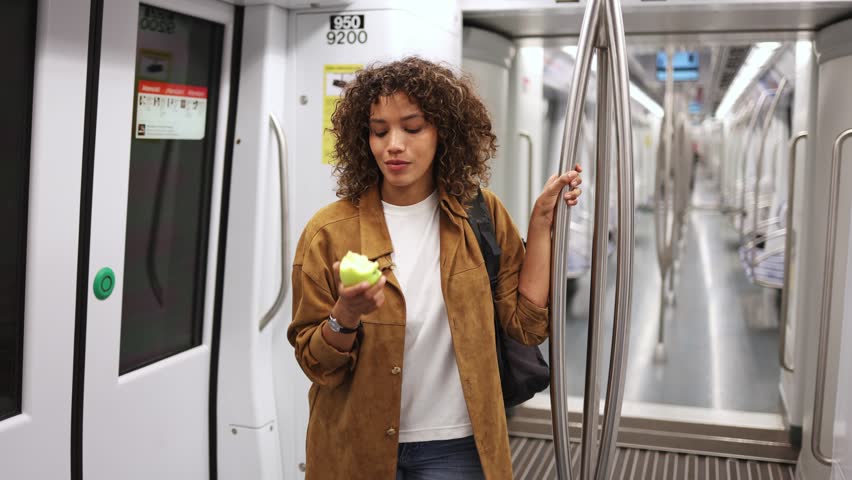Young woman eating green apple in subway in slow motion. Young woman stands by the subway door, enjoying a green apple while captured in slow motion