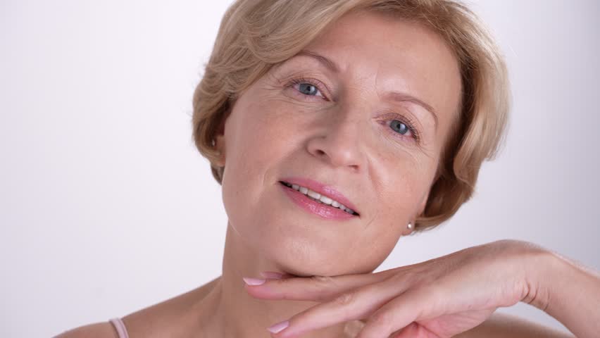 Closeup portrait of a confident woman in her 50s is gently touching her face, celebrating the beauty of graceful aging and selflove
