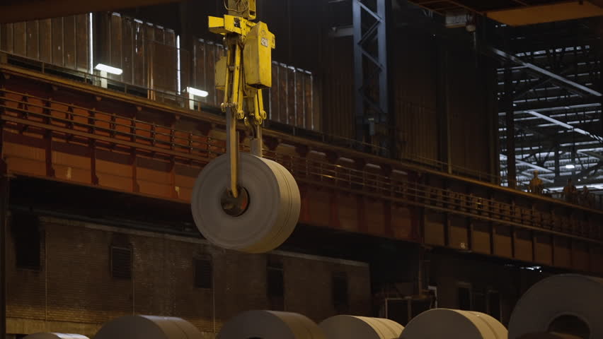 In an industrial warehouse environment, a crane skillfully lifts large steel coils for various operations and logistics