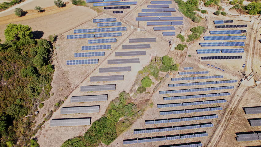 An expansive layout of solar panels captures sunlight in a rural setting, surrounded by grassy patches, with neat rows stretching across the landscape during daylight.
