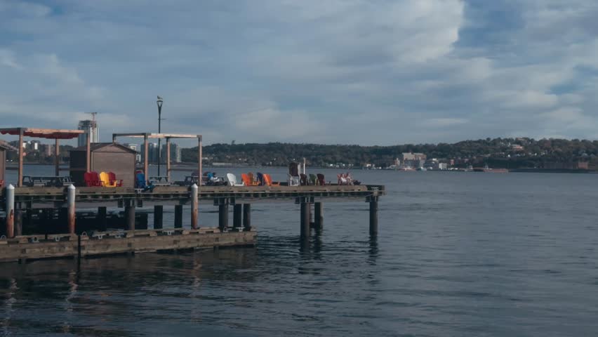  People relax on a pier on a sunny day, lying on deck chairs as a boat sails past them. Halifax, Canada.
