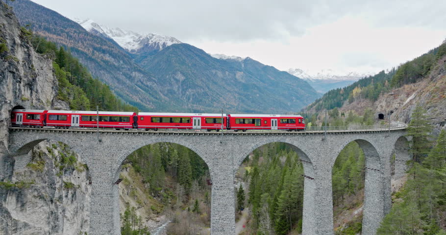 Landwasser Viaduct world heritage sight with luxury Glacier and Bernina express in Swiss Alps summer autumn scenery. Aerial Drone shot red train passing through famous mountain in Filisur, Switzerland