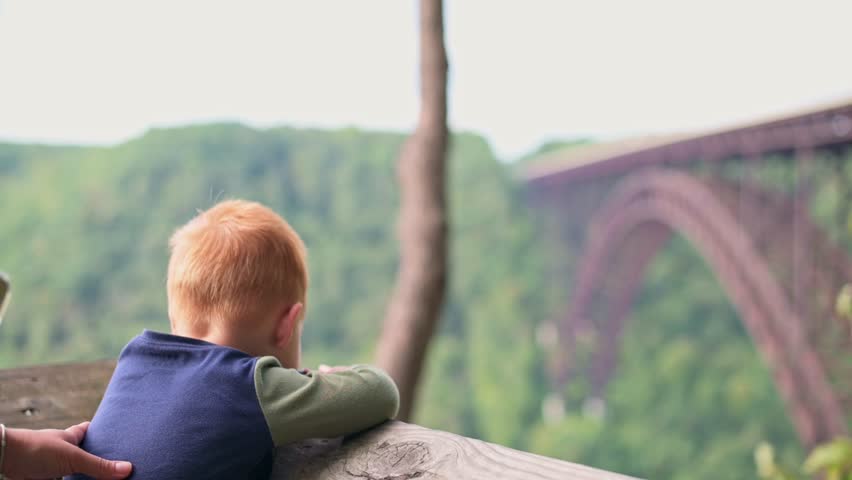 young child and their parent share moment of awe, pointing at New River Gorge Bridge in distance, surrounded by lush greenery and natural beauty New River Gorge Bridge child and their parent