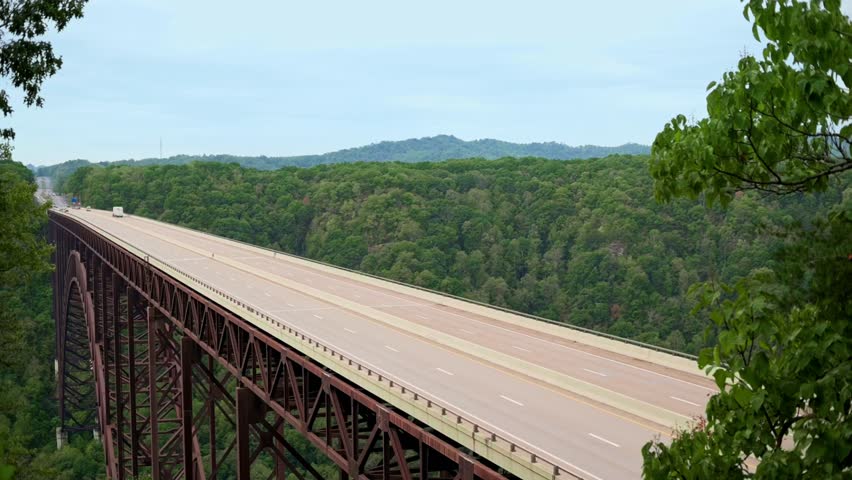 New River Gorge Bridge stretches over forested valley in West Virginia, showcasing its steel structure and open highway with lush green mountains in background. New River Gorge Bridge USA