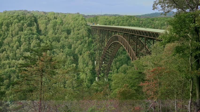 wide-angle view of the New River Gorge Bridge stretching across a lush, green valley in West Virginia, showcasing its stunning steel architecture amid a breathtaking natural setting