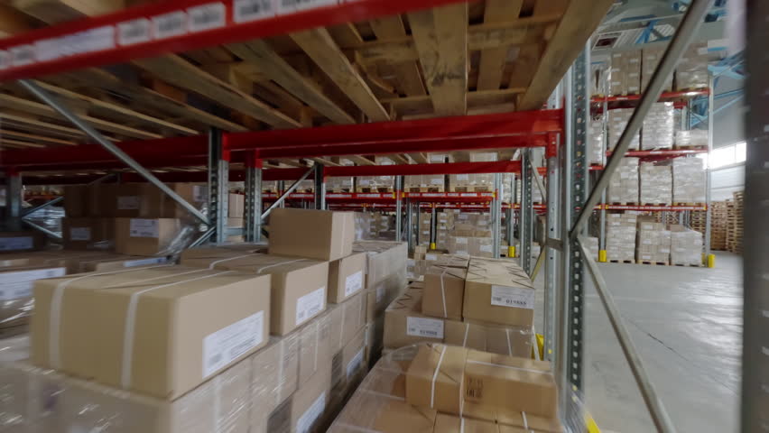 Tall steel shelves packed with cardboard boxes define warehouse interior. Boxes arranged in orderly manner making inventory management efficient FPV