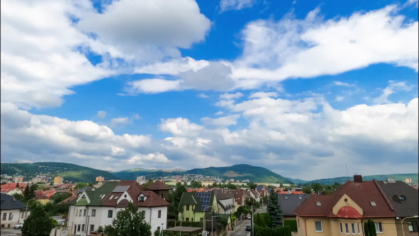Picturesque scenery of cozy urban landscape, mountains and amazing clouds spreading by the sky. Low angle view at cumulus cloudscape in summer. Timelapse.