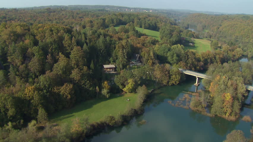 Flying over a river with a bridge in beautiful green landscape with houses