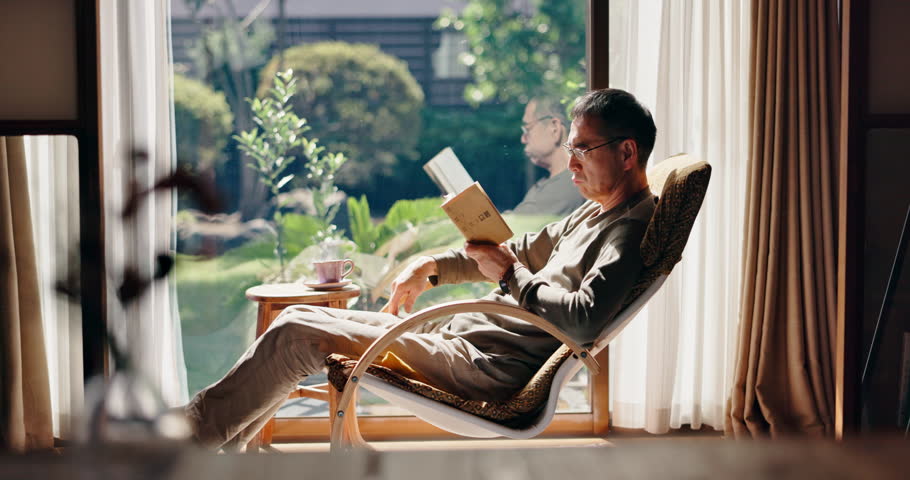 Chair, tea or mature man in home reading book for rest break, retirement or novel to relax alone. Reader, coffee or Japanese person drinking beverage with fiction story or peace for fantasy or hobby