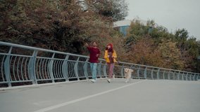 Happy multiracial couple runs with dog on city footbridge. Joyful diverse friends jogs alongside with golden retriever laughing and having fun in autumn - Powered by Shutterstock - Get 15% off with code: PIKWIZARD15