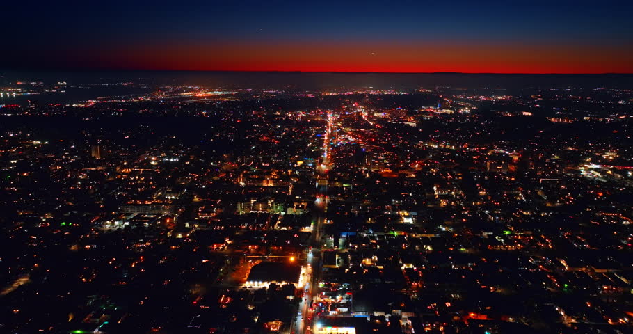 Flight above the straight highway crossing the panorama of a big city. Aerial perspective on the scenery of San Diego, California, the USA. Red sky above the metropolis.