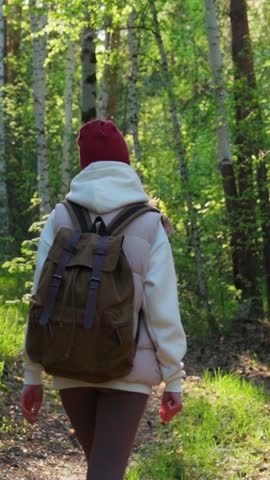 A woman walking along a forest path on a sunny day. Hiking in nature, traveling, outdoors. Hiking. Vertical video, shorts.