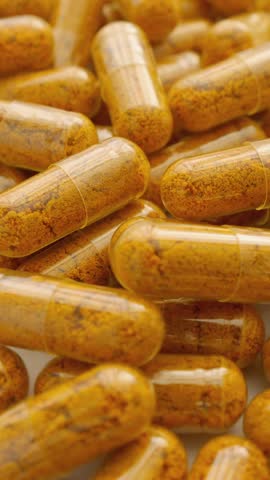Orange capsules of turmeric dietary supplement with pepper. Capsule collection on white background, spinning to rhythm health. Path to Healthy Life: Pharmaceutical Industry in Production of Capsules.