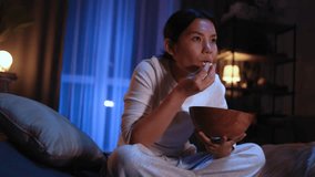 Addicted focused young asian woman looking at screen while watching interesting TV program film movie and eating popcorn at home Enchanted brunette girl cannot take her eyes off at late night indoors - Powered by Shutterstock - Get 15% off with code: PIKWIZARD15