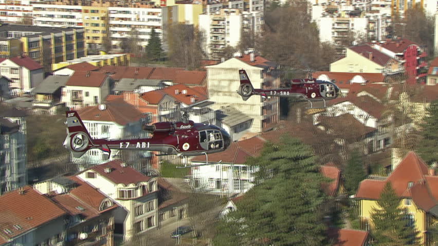 Two helicopters flying close together low over buildings in urban area. Aerial