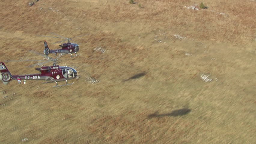 Aerial shot of two helicopters flying close together low over a mountain