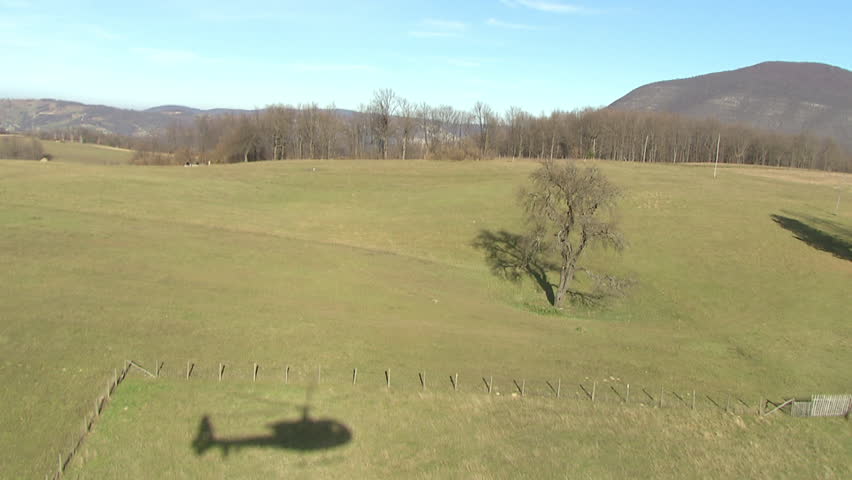 Two helicopters flying close together in rural environment near mountains.