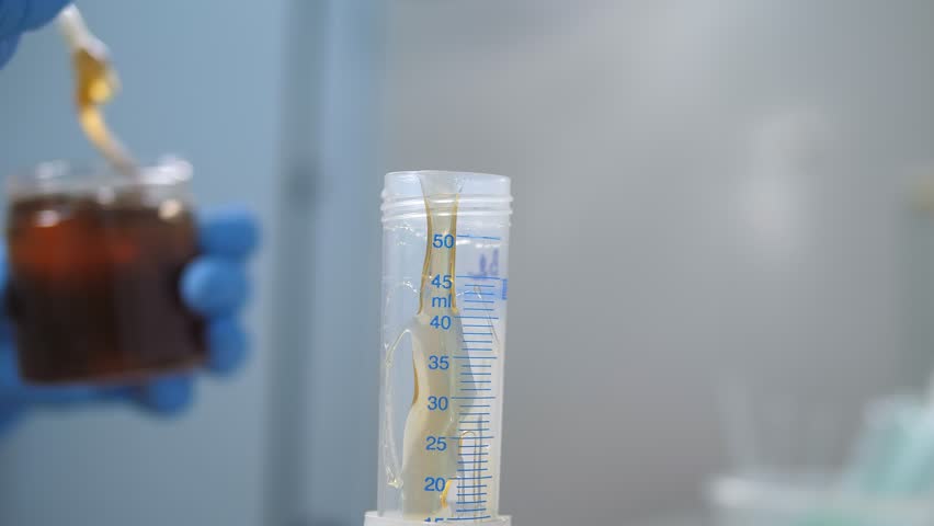 A close-up of a laboratory assistant pouring honey into a test tube with a scale in a laboratory at production. Checking the quality of natural honey.