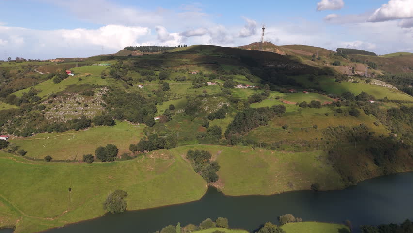 An aerial view of Loiolako lake between lush hills in Basque Country, Bilbao, Spain. Piruli Argalario seen in a distance with blue sky
