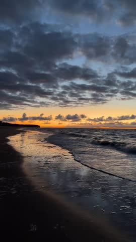 Pittoresque sunset recording the waves of the baltic sea crushing onto the sandy beach with many clouds in the orange sunset sky. 