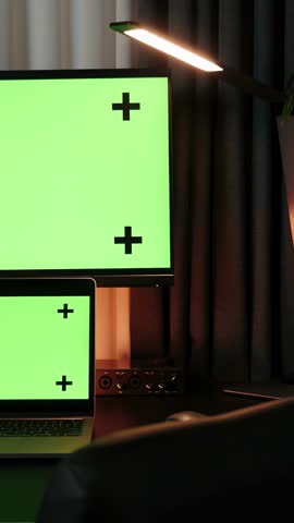 Personal computer and laptop with mock-up green screen monitors stand on office desk. Stylish creative home office workplace. Business concept. Vertical video