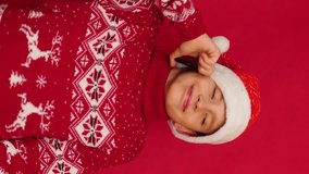 cheerful dancing Caucasian boy 10 years old in Santa hat and New Year red sweater talking on phone congratulating on New Year and Christmas, vertical video, red studio background - Powered by Shutterstock - Get 15% off with code: PIKWIZARD15
