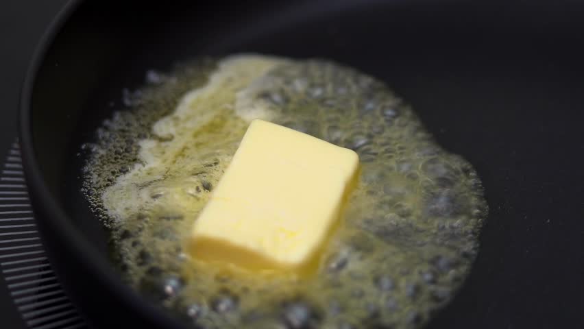 Close up of fresh butter melts and sizzles in hot frying pan on stove. Cooking food. Concept non-stick pan