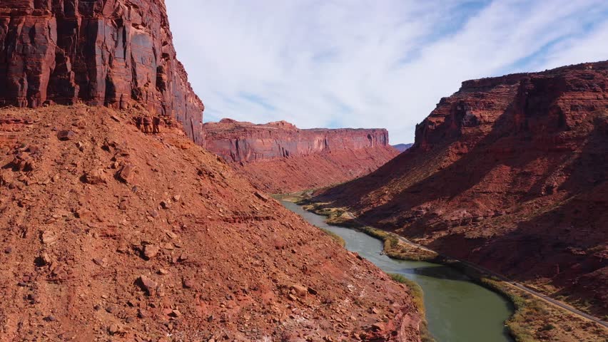 Aerial view across stunning canyon, revealing a Colorado river flowing gracefully between impressive red rock formations and towering cliffs on either side. Road passing near river bank. Usa nature