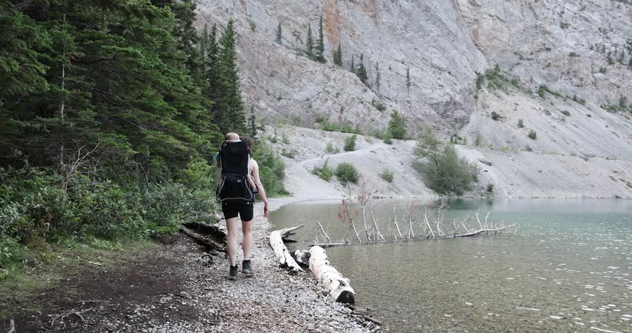 A mother hikes with a baby on her back along a mountain lake. She is enjoying her hike. Crowsnest Pass, Alberta, Canada.