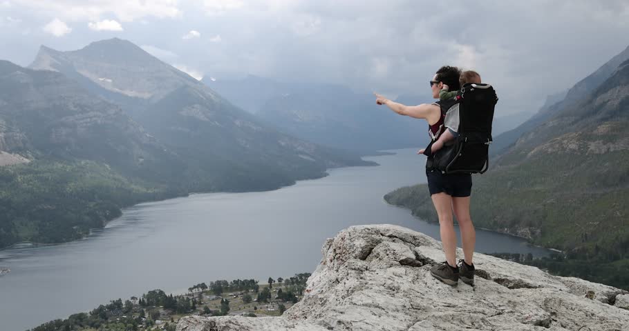 A mother bonds with her baby while overlooking a beautiful mountain lake after a hike. Waterton National Park, Alberta, Canada.
