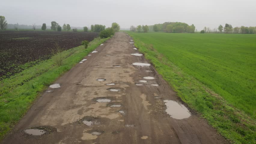 bad rural road with the lot of pits holes and puddles after the rain
