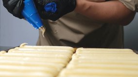 A pastry chef makes eclairs in a bakery. eclairs are baked in the oven. eclair production process. pastry bag with dough - Powered by Shutterstock - Get 15% off with code: PIKWIZARD15