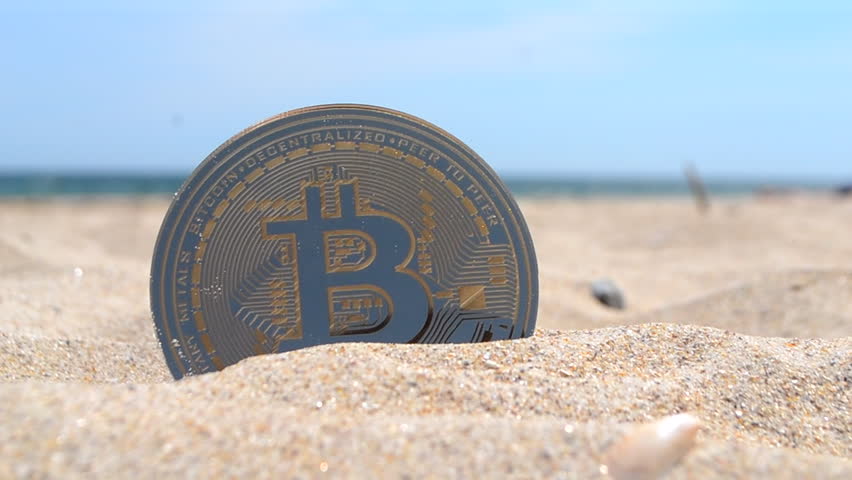 Bitcoin BTC coin close up. Bitcoin BTC coin half buried in the sand on the sandy beach with the blue sky of the seashore on a sunny summer day. Concept cryptocurrency web 3 cryptocurrencies crypto