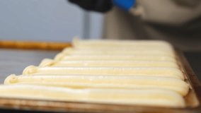 A pastry chef makes eclairs in a bakery. eclairs are baked in the oven. eclair production process. pastry bag with dough - Powered by Shutterstock - Get 15% off with code: PIKWIZARD15