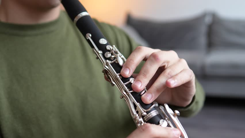Clarinet player closeup. Clarinetist hands playing flute woodwind music instrument at home, selective focus. Musical instruments. Guy plays the oboe in education classroom. Hobby. 